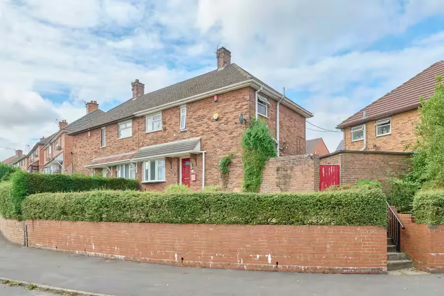 A brick semi-detached house behind a hedge and low wall